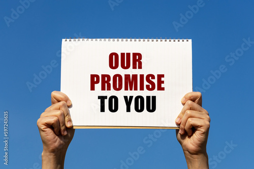 Bild auf Leinwand Our promise to you text on notebook paper held by 2 hands with isolated blue sky background
