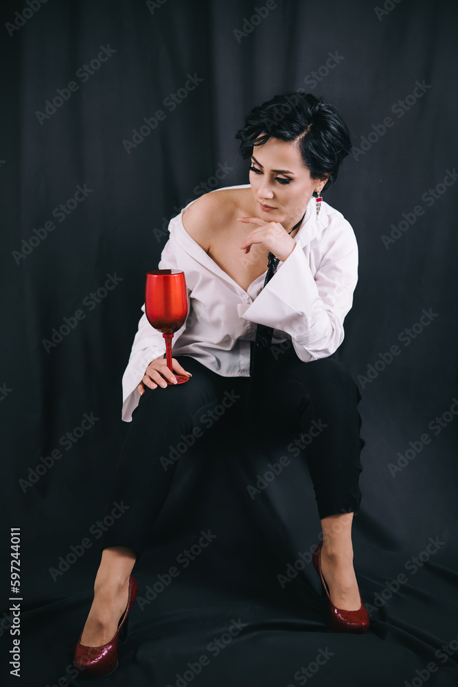Stylish shot of young fashionable lady in white shirt holding decorative drinking glass and posing for camera