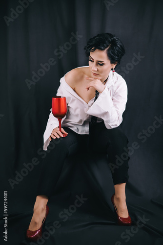 Obraz na płótnie Stylish shot of young fashionable lady in white shirt holding decorative drinking glass and posing for camera w salonie