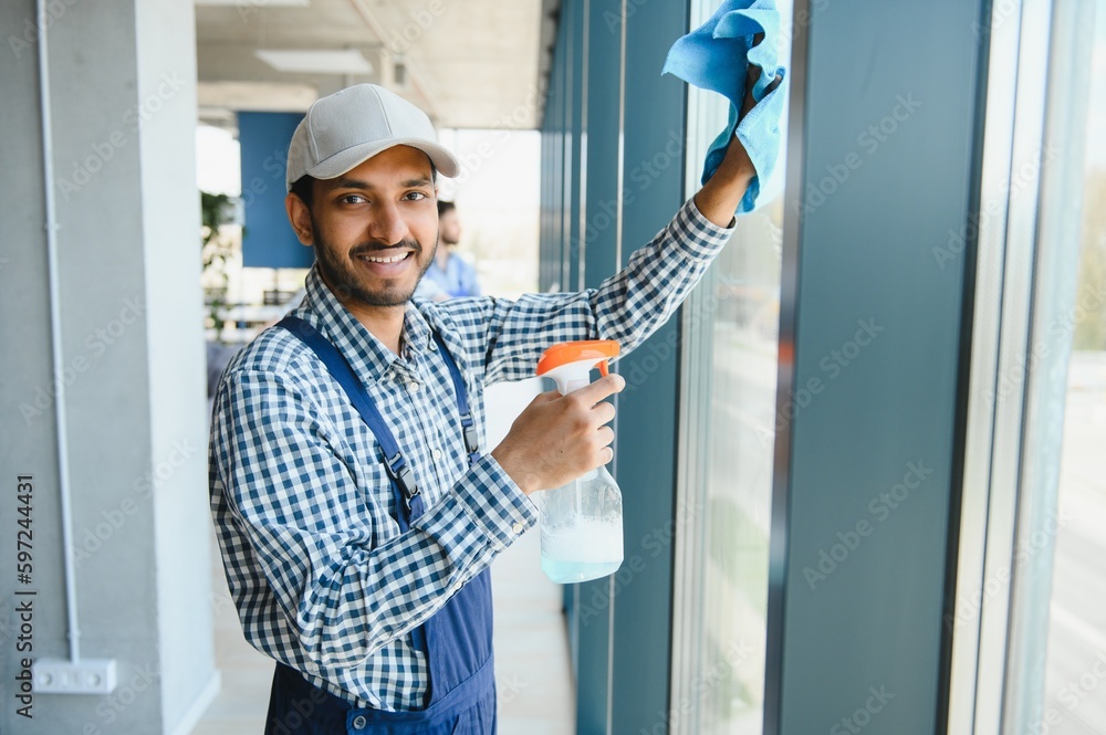 Young indian man washing window in office. Young indian man washing window in office.