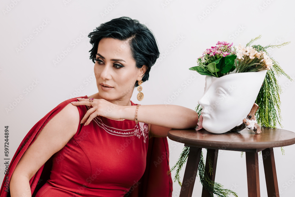 Spring portrait of young woman in elegant red dress posing with plaster head vase with flowers