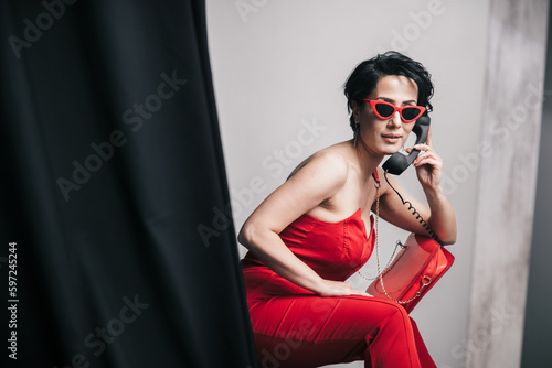 Fashionable young lady in red dress talking on non-functional toy phone and holding her glamorous clutch