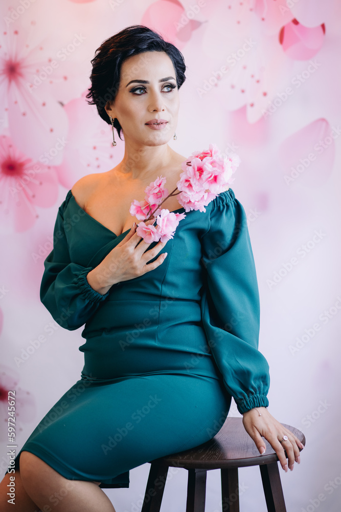 A young elegant womman sitting on chair and posing for camera holding pink flower