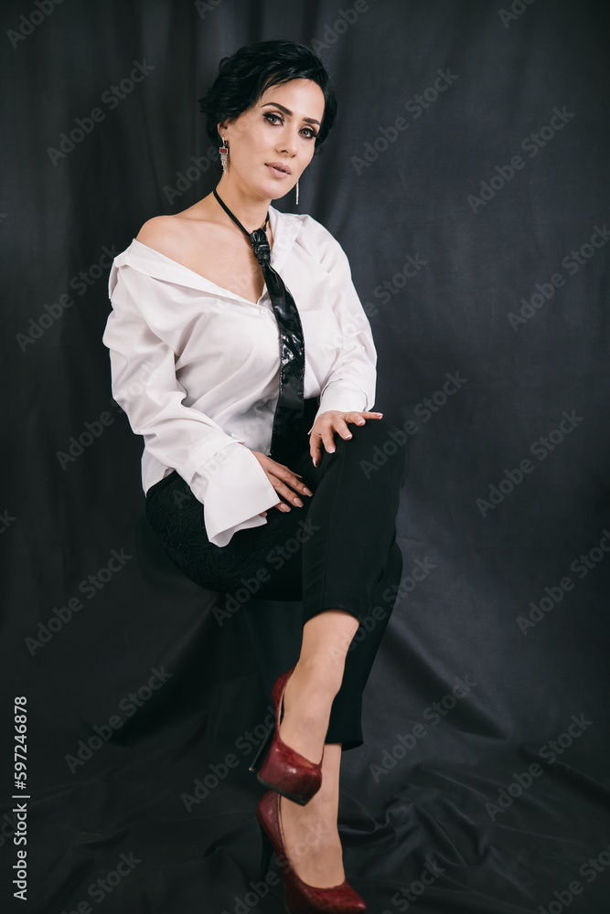 Young confident woman sitting on the chair in studio with black background in white shirt