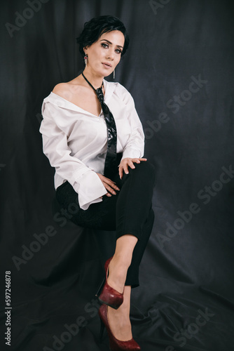 Obraz na płótnie Young confident woman sitting on the chair in studio with black background in white shirt w salonie