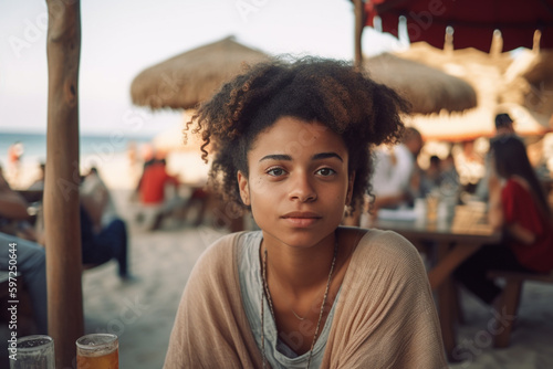 young adult woman or teenager outside in free time, sitting alone at a table at the beach, curly hair tanned skin slim figure. Generative AI #597250644