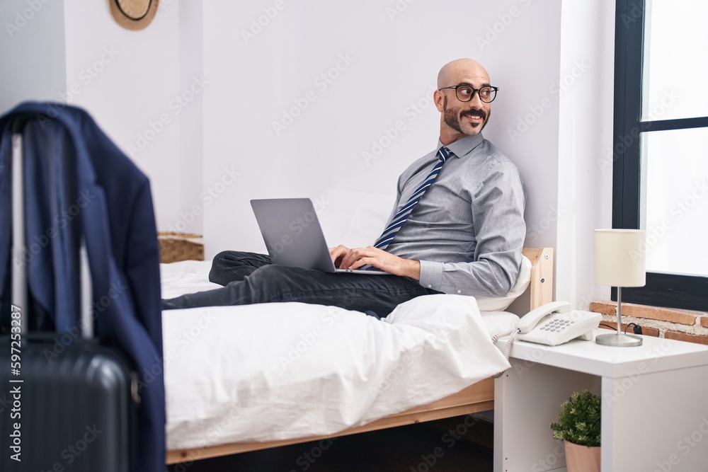 Young hispanic man business worker using laptop sitting on bed at hotel room Young hispanic man business worker using laptop sitting on bed at hotel room