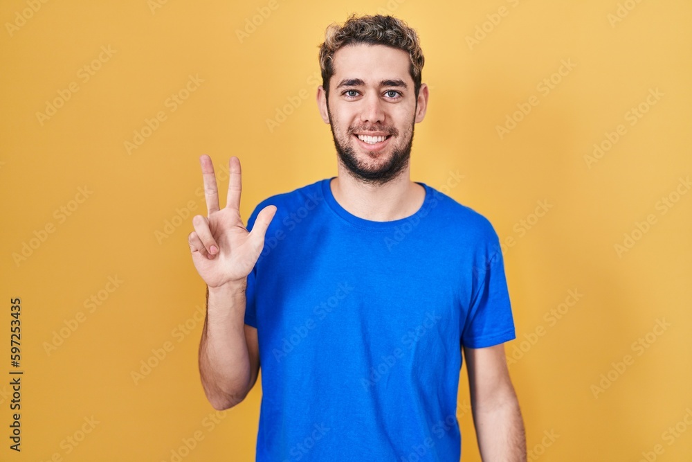 Fototapeta premium Hispanic man with beard standing over yellow background showing and pointing up with fingers number three while smiling confident and happy.