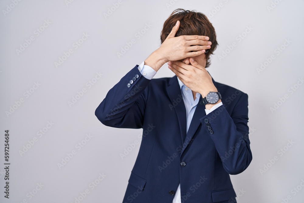 Hispanic business young man wearing glasses covering eyes and mouth with hands, surprised and shocked. hiding emotion Hispanic business young man wearing glasses covering eyes and mouth with hands, surprised and shocked. hiding emotion