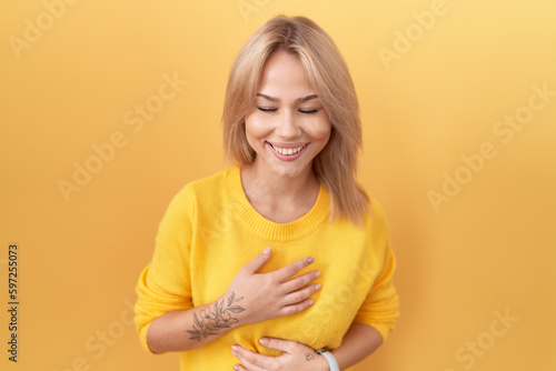 Young caucasian woman wearing yellow sweater smiling and laughing hard out loud because funny crazy joke with hands on body.