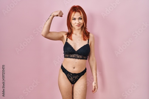 Young caucasian woman wearing lingerie over pink background strong person showing arm muscle, confident and proud of power