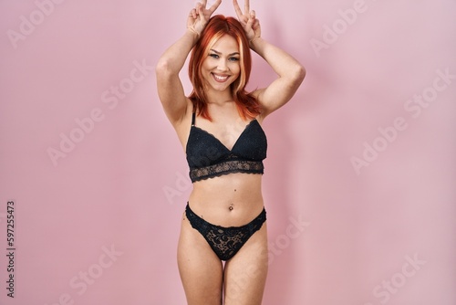 Young caucasian woman wearing lingerie over pink background posing funny and crazy with fingers on head as bunny ears, smiling cheerful