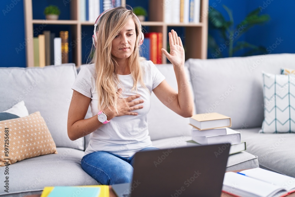 Young blonde woman studying using computer laptop at home swearing with hand on chest and open palm, making a loyalty promise oath Young blonde woman studying using computer laptop at home swearing with hand on chest and open palm, making a loyalty promise oath