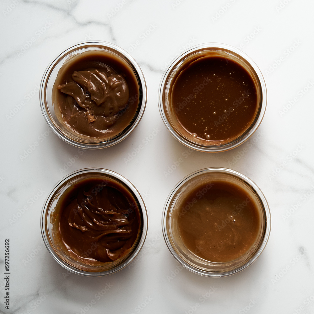 Four Different Salted Caramel sauces in glass bowls on white marble background. Butter, sugar with cream and salt. Top view Four Different Salted Caramel sauces in glass bowls on white marble background. Butter, sugar with cream and salt. Top view