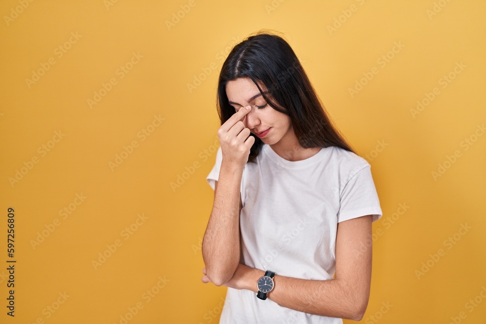 Young beautiful woman standing over yellow background tired rubbing nose and eyes feeling fatigue and headache. stress and frustration concept. Young beautiful woman standing over yellow background tired rubbing nose and eyes feeling fatigue and headache. stress and frustration concept.