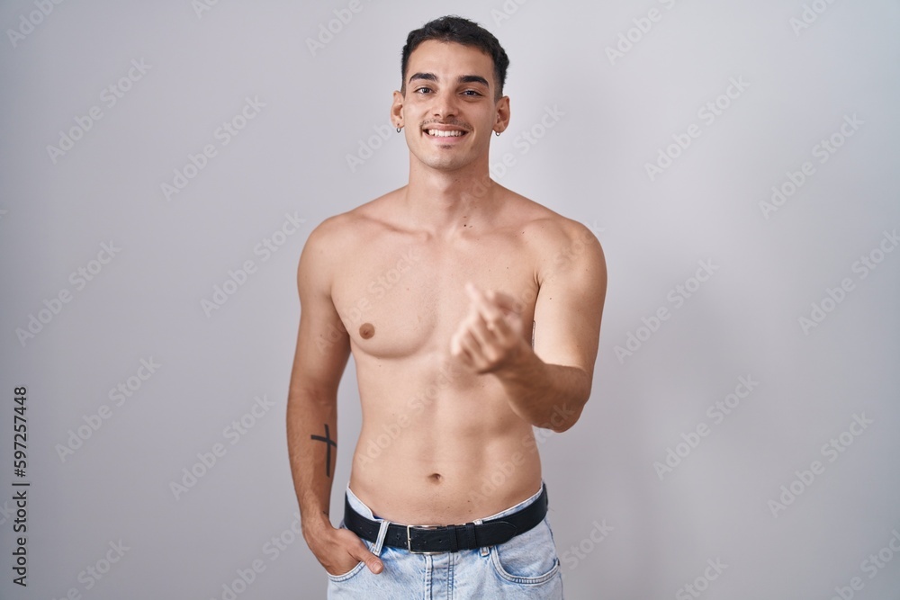 Handsome hispanic man standing shirtless beckoning come here gesture with hand inviting welcoming happy and smiling