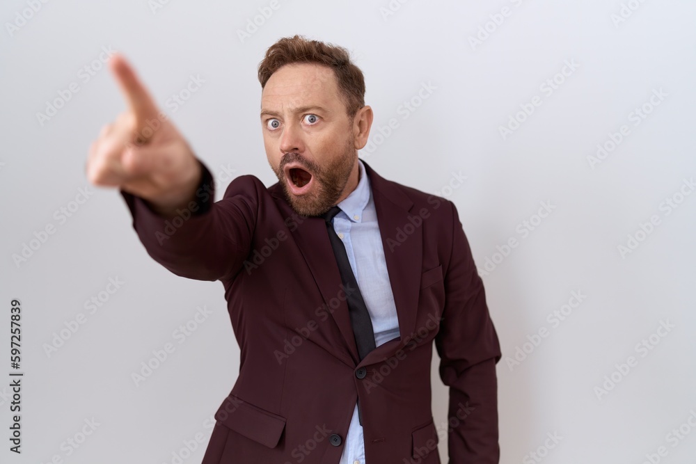 Middle age business man with beard wearing suit and tie pointing with finger surprised ahead, open mouth amazed expression, something on the front Middle age business man with beard wearing suit and tie pointing with finger surprised ahead, open mouth amazed expression, something on the front