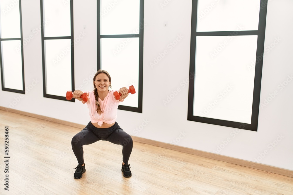 Fototapeta premium Young beautiful hispanic woman smiling confident using dumbbells training at sport center
