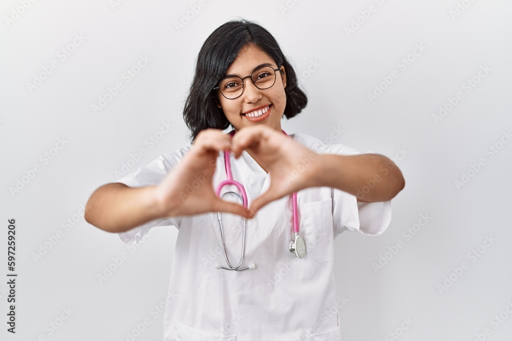 Young hispanic doctor woman wearing stethoscope over isolated background smiling in love doing heart symbol shape with hands. romantic concept. Young hispanic doctor woman wearing stethoscope over isolated background smiling in love doing heart symbol shape with hands. romantic concept.