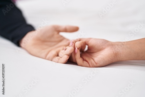 Man and woman couple lying on bed with hands together at bedroom