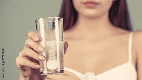 Woman taking drugs to releave headache. Woman take some pills, holds glass of water. Young woman taking pill against headache. Girl taking a pill with a glass of water photo