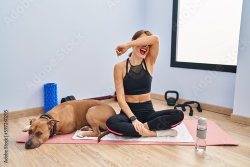 Young beautiful woman sitting on yoga mat smiling cheerful playing peek a boo with hands showing face. surprised and exited