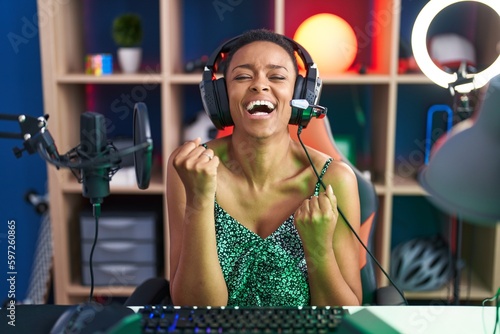 African american woman playing video games very happy and excited doing winner gesture with arms raised, smiling and screaming for success. celebration concept.