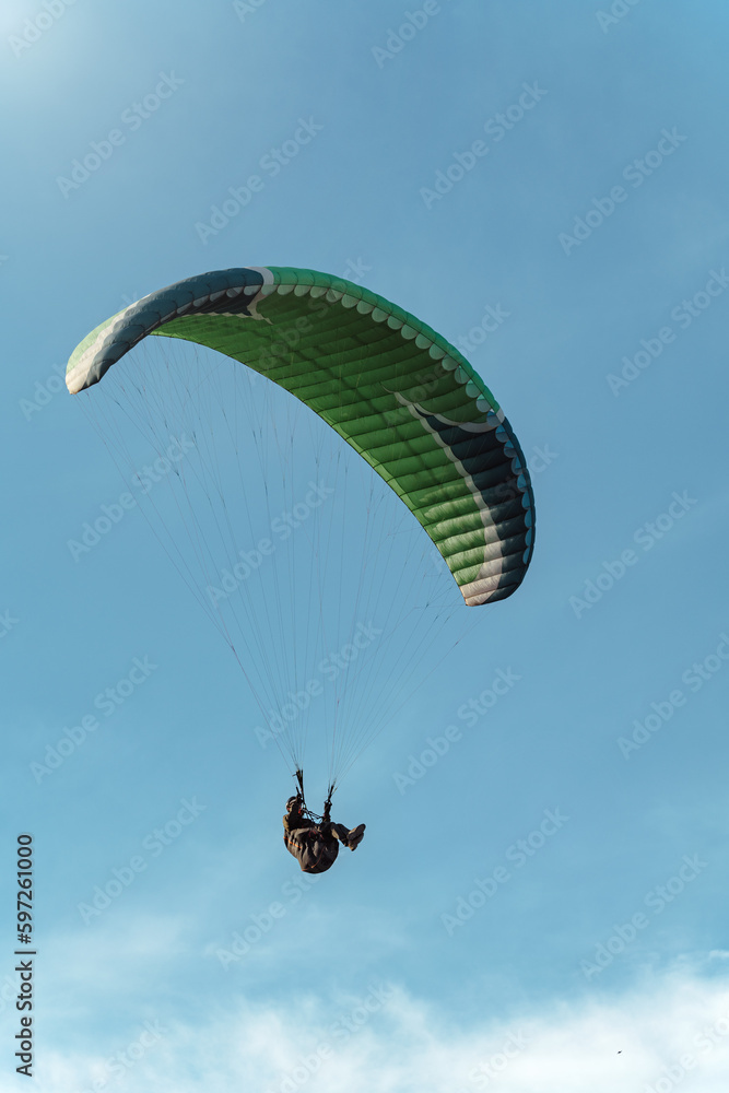 Bottom view of green paraglider flying among blue sky on a sunny day. Bottom view of green paraglider flying among blue sky on a sunny day.