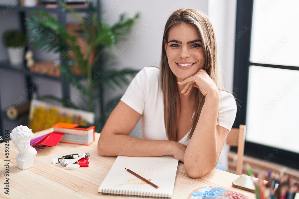 Young woman artist smiling confident sitting on desk at art studio Young woman artist smiling confident sitting on desk at art studio