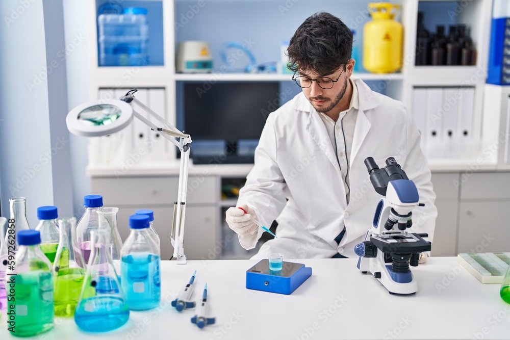 Young hispanic man scientist measuring liquid at laboratory Young hispanic man scientist measuring liquid at laboratory