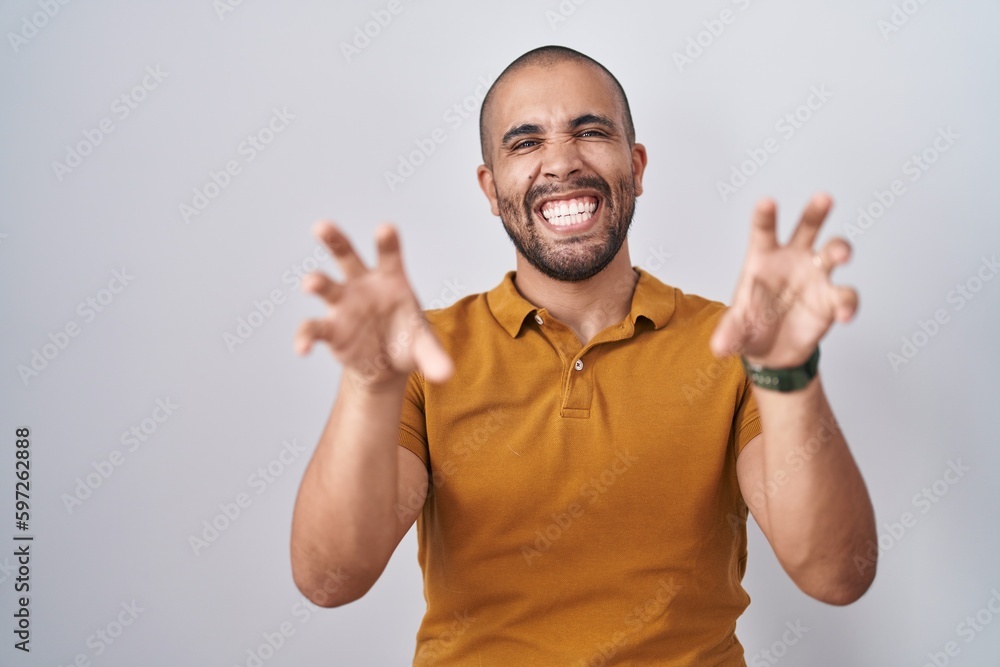 Hispanic man with beard standing over white background smiling funny doing claw gesture as cat, aggressive and sexy expression Hispanic man with beard standing over white background smiling funny doing claw gesture as cat, aggressive and sexy expression