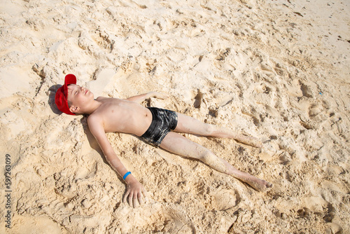 Oudoor summer activity. Concept of fun, health and vacation. Happy boy eight years old relax and liing on warm sand on a hot summer day near the ocean. Cancun, Mexico.