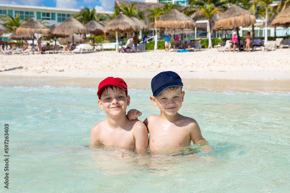 Oudoor summer activity. Concept of fun, health and vacation. Happy bothers boys eight and five years old relax and swimming on warm ocean on a hot summer day in a resort. Cancun, Mexico.