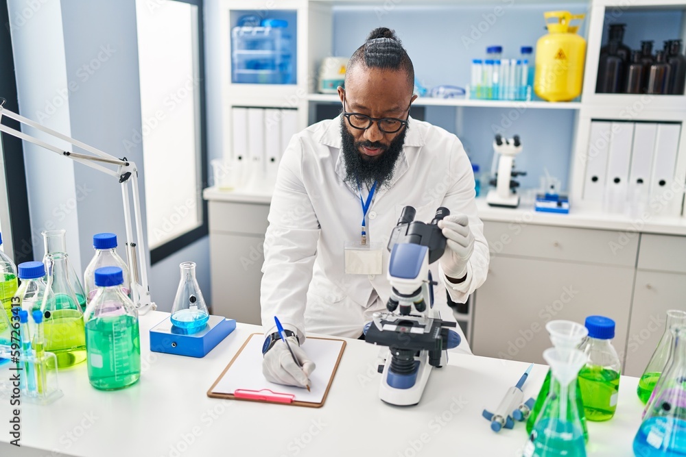 Young african american man wearing scientist uniform using microscope at laboratory Young african american man wearing scientist uniform using microscope at laboratory