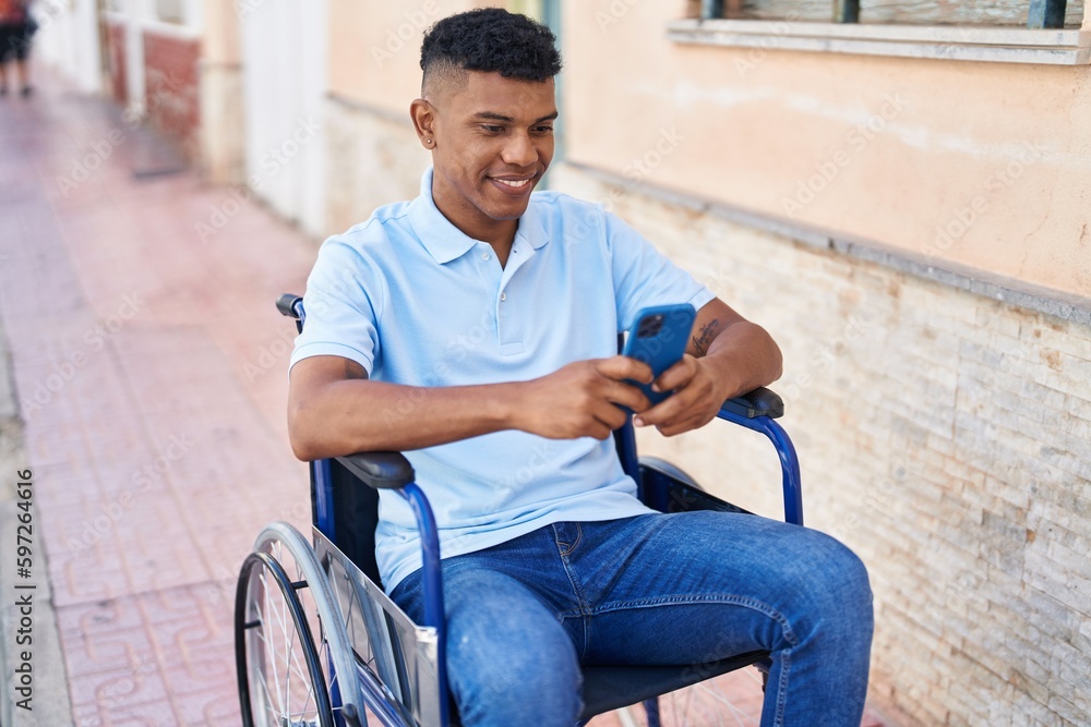 Young latin man using smartphone sitting on wheelchair at street