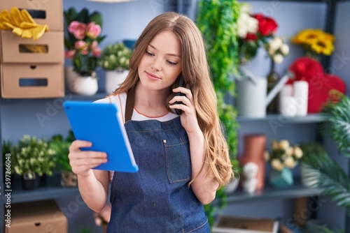 Young woman florist talking on smartphone using touchpad at florist shop