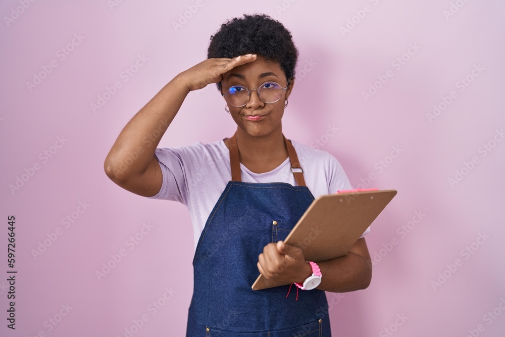 Young african american woman wearing professional waitress apron holding clipboard worried and stressed about a problem with hand on forehead, nervous and anxious for crisis Young african american woman wearing professional waitress apron holding clipboard worried and stressed about a problem with hand on forehead, nervous and anxious for crisis