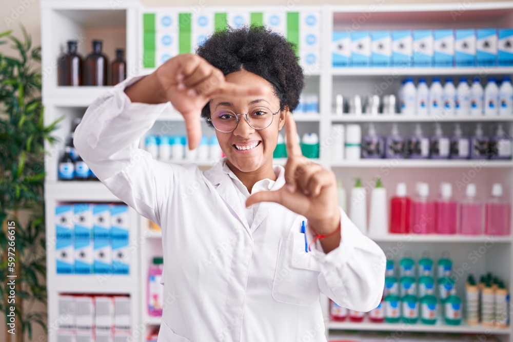 Beautiful african woman with curly hair working at pharmacy drugstore smiling making frame with hands and fingers with happy face. creativity and photography concept. Beautiful african woman with curly hair working at pharmacy drugstore smiling making frame with hands and fingers with happy face. creativity and photography concept.