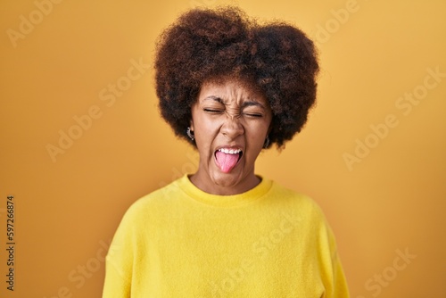 Young african american woman standing over yellow background sticking tongue out happy with funny expression. emotion concept. © Krakenimages.com