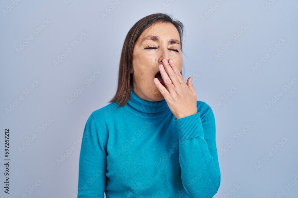 Middle age hispanic woman standing over isolated background bored yawning tired covering mouth with hand. restless and sleepiness. Middle age hispanic woman standing over isolated background bored yawning tired covering mouth with hand. restless and sleepiness.