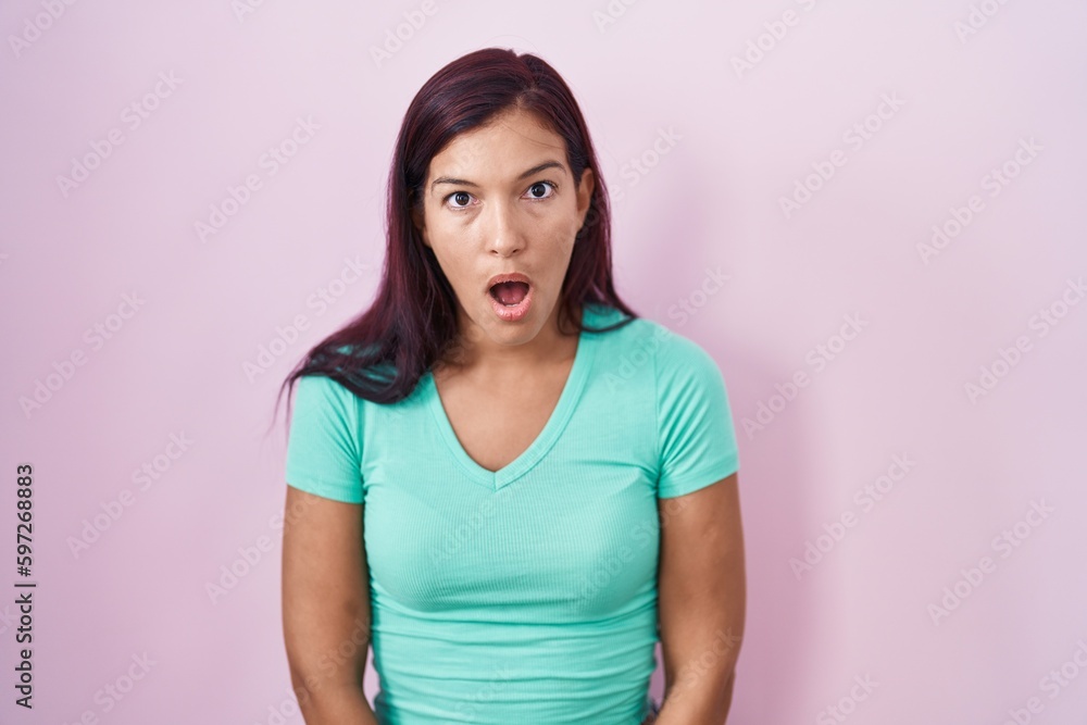 Young hispanic woman standing over pink background afraid and shocked with surprise and amazed expression, fear and excited face. Young hispanic woman standing over pink background afraid and shocked with surprise and amazed expression, fear and excited face.