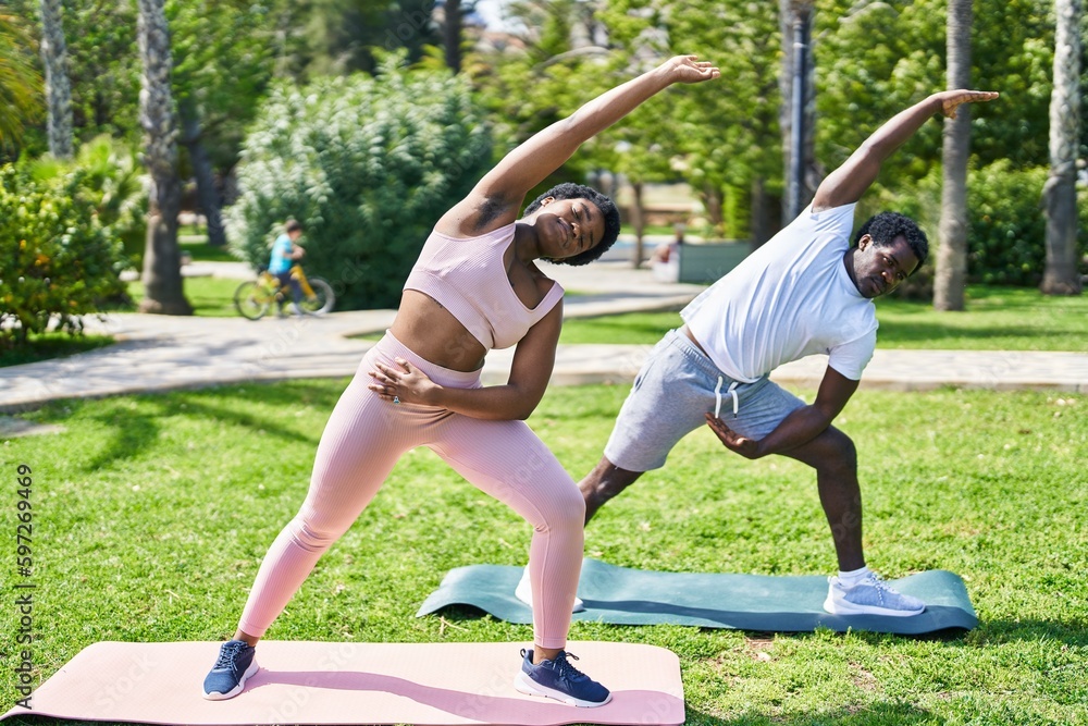 Fototapeta premium African american man and woman couple doing yoga exercise at park
