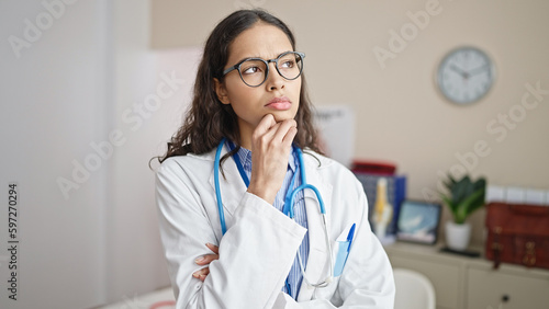 Young beautiful hispanic woman doctor standing with doubt expression thinking at clinic