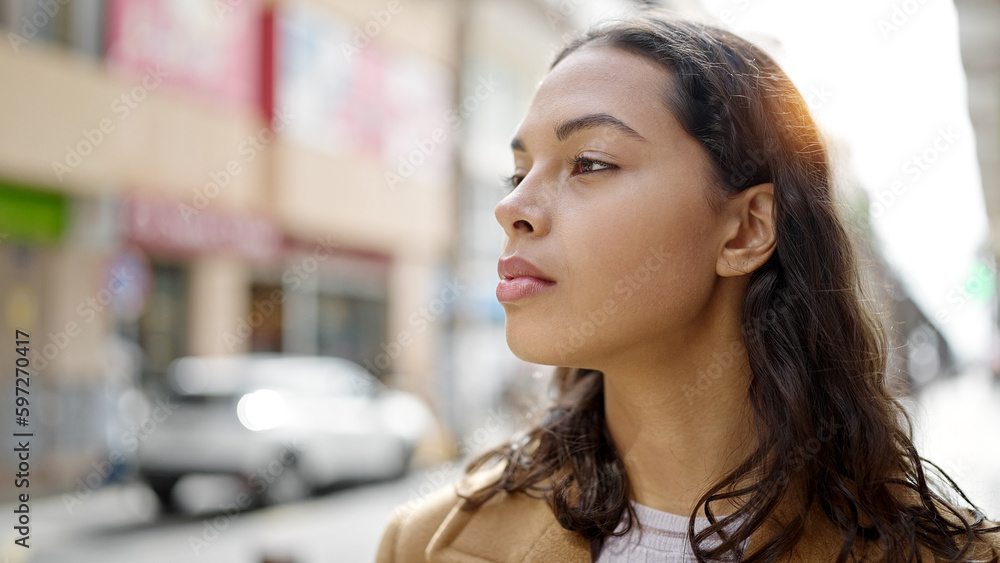 Young beautiful hispanic woman standing with serious expression looking to the side at street