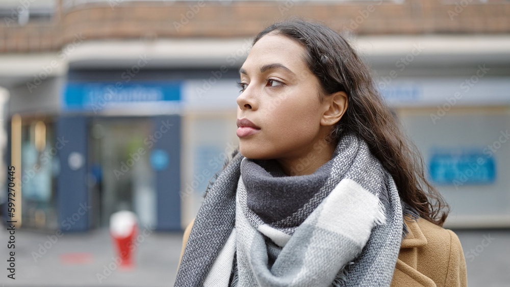 Young beautiful hispanic woman standing with serious expression looking to the side at street