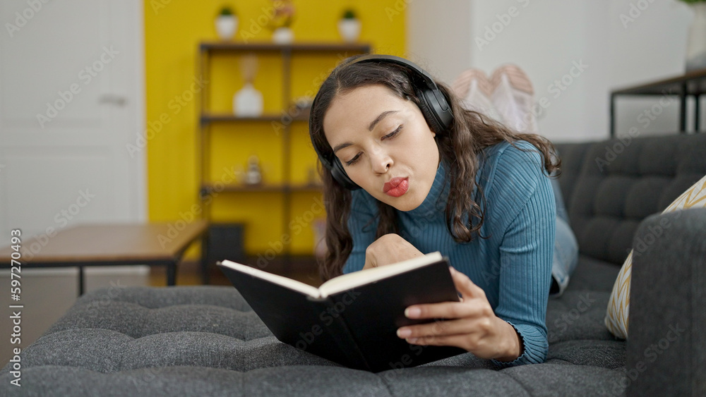 Young beautiful hispanic woman reading book lying on sofa wearing headphones at home Young beautiful hispanic woman reading book lying on sofa wearing headphones at home