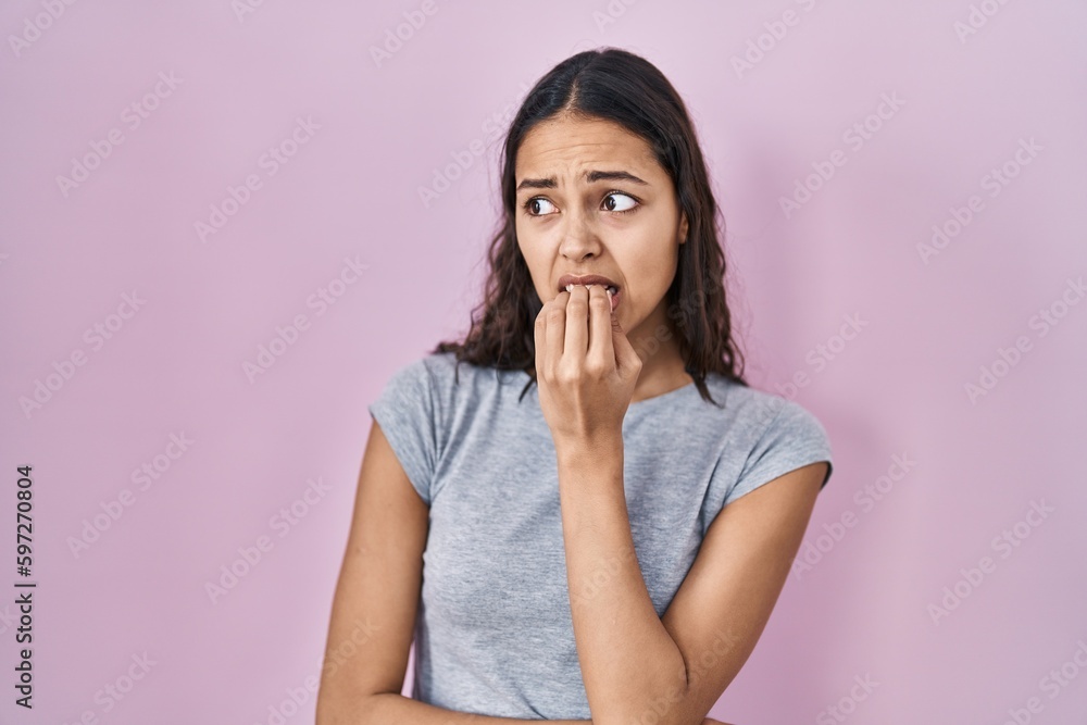 Young brazilian woman wearing casual t shirt over pink background looking stressed and nervous with hands on mouth biting nails. anxiety problem. Young brazilian woman wearing casual t shirt over pink background looking stressed and nervous with hands on mouth biting nails. anxiety problem.