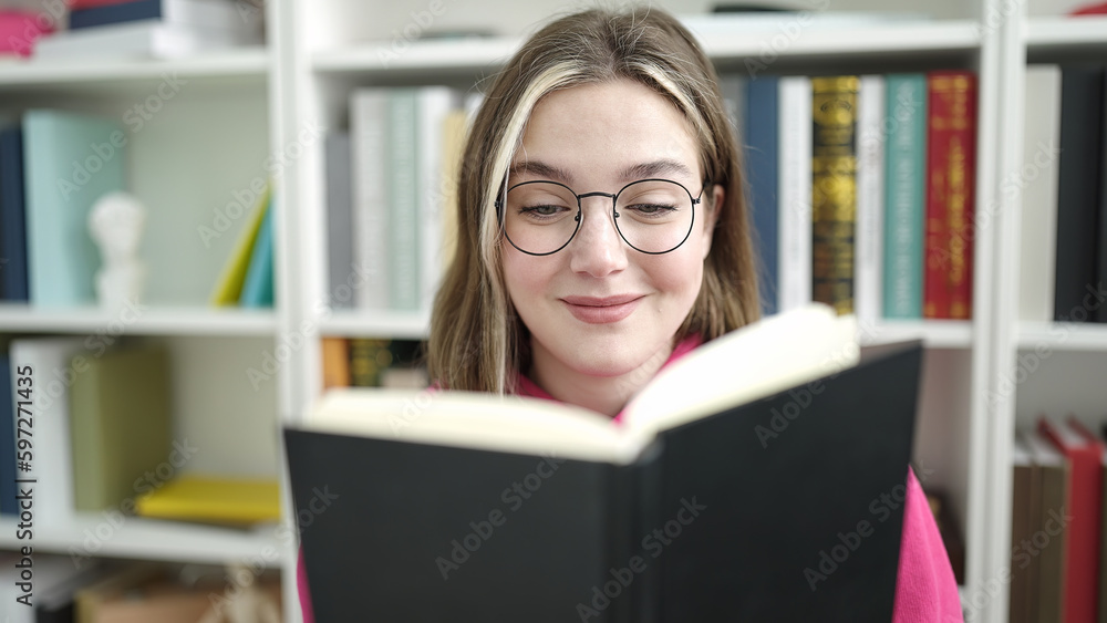 Young blonde woman student reading book sitting on table at library university Young blonde woman student reading book sitting on table at library university