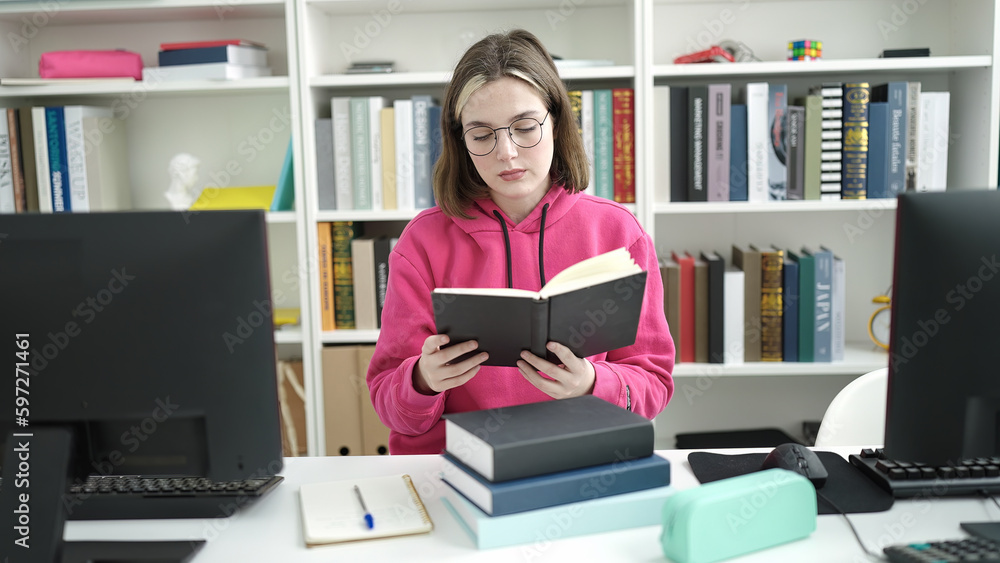 Young blonde woman student reading book sitting on table at library university Young blonde woman student reading book sitting on table at library university