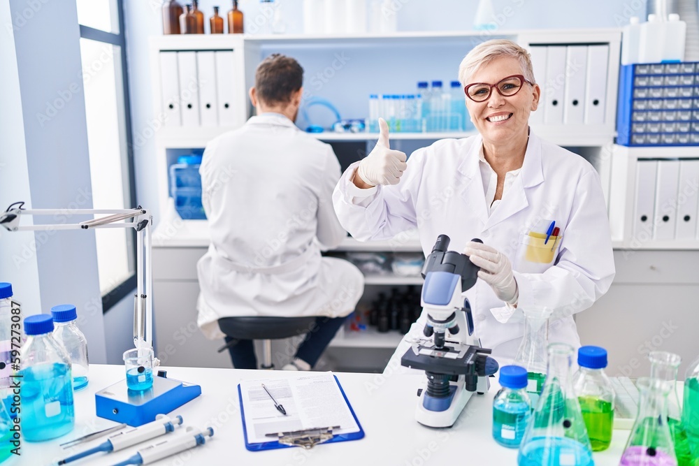 Middle age woman working at scientist laboratory smiling happy and positive, thumb up doing excellent and approval sign Middle age woman working at scientist laboratory smiling happy and positive, thumb up doing excellent and approval sign